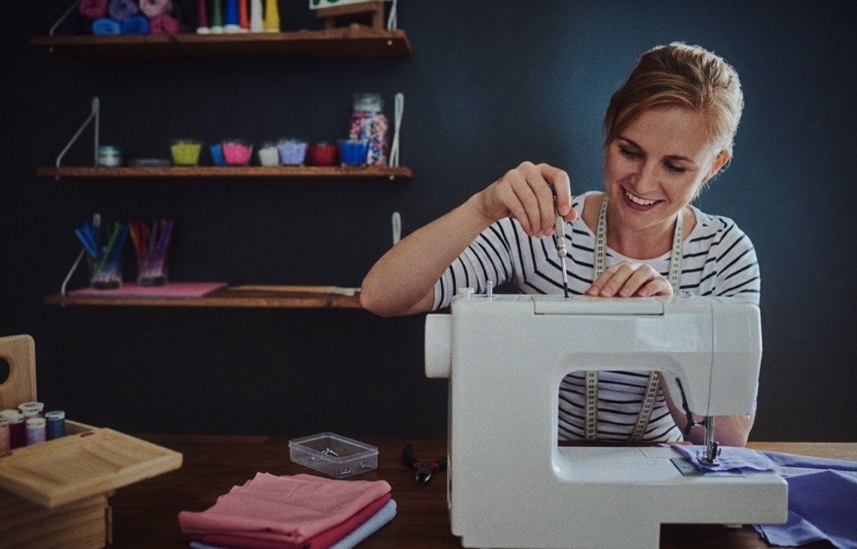 A sewist smiling as she services her sewing machine at a bright studio desk